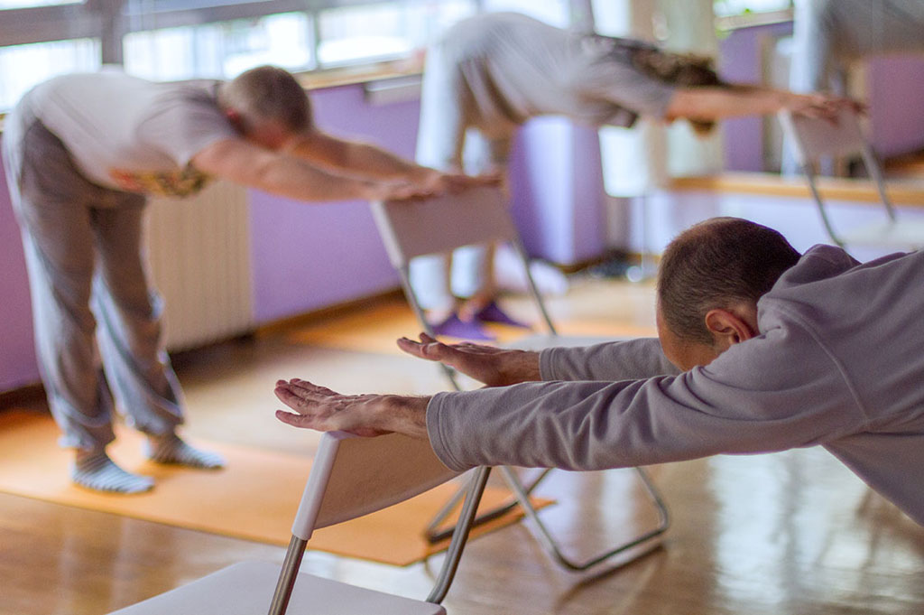 Chair yoga class with participants doing gentle forward stretch using chairs at Yoga with Ashleigh